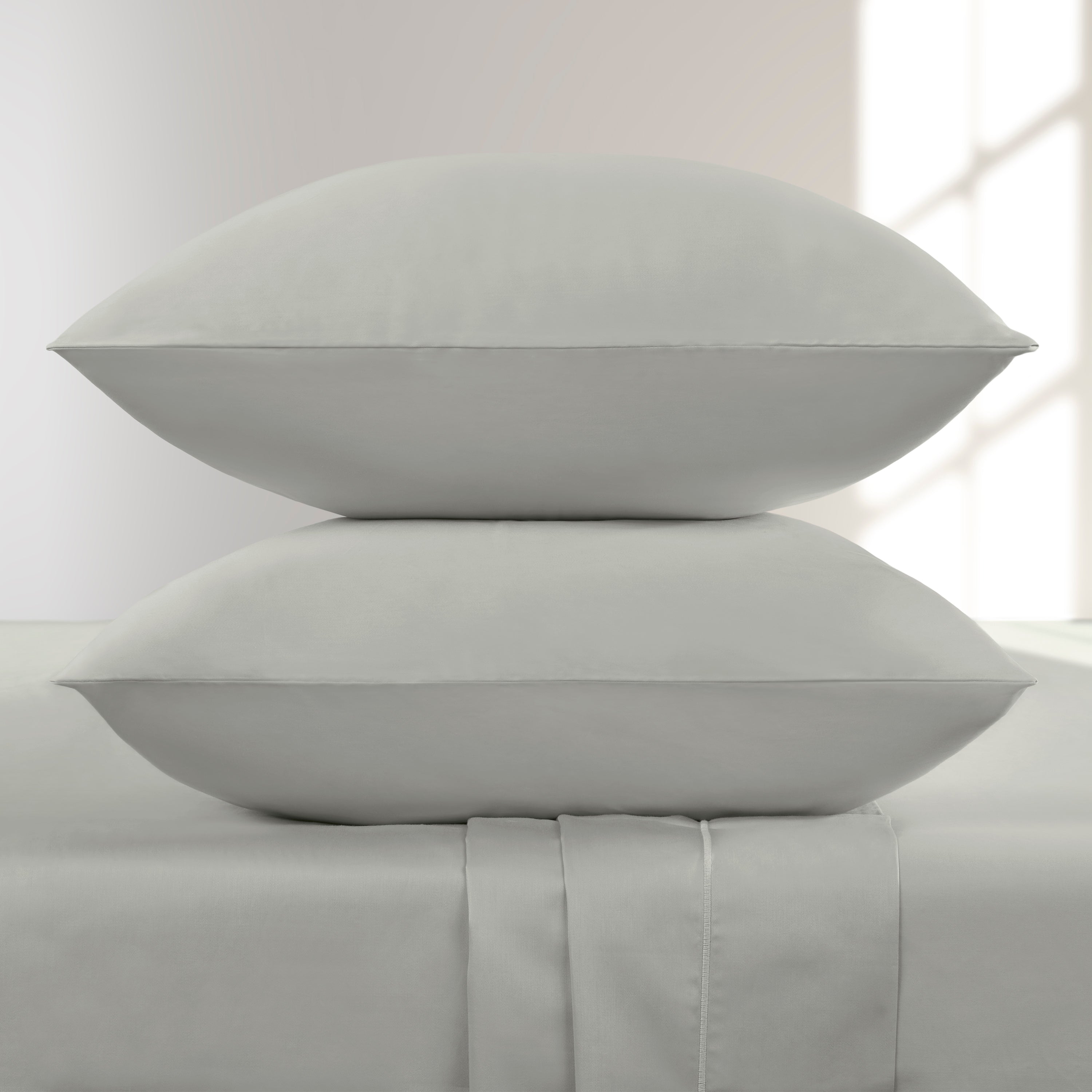 Two Oystershell pillows stacked on a bed with a light background