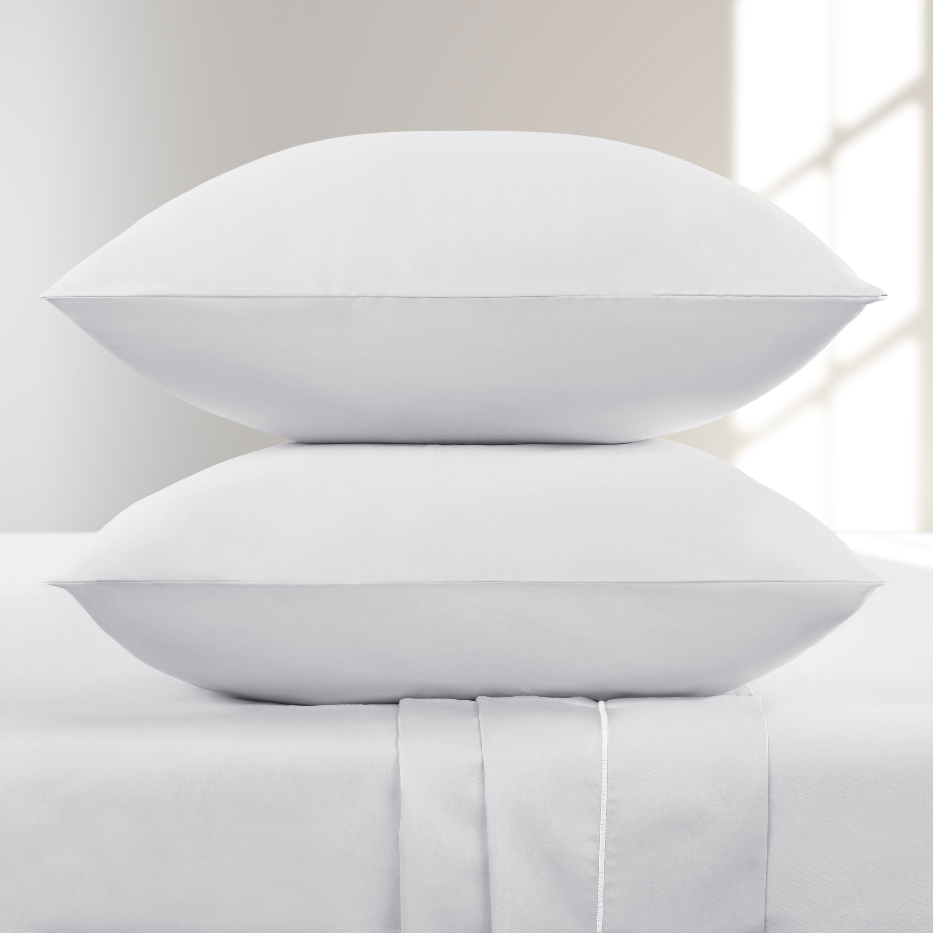 Two white pillows stacked on a bed with a neutral background
