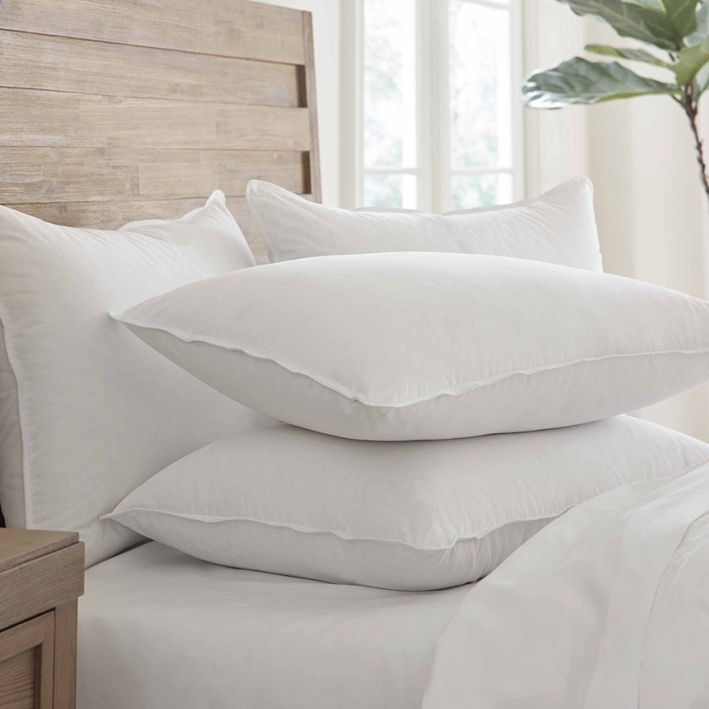 Stack of white pillows on a bed with a wooden headboard and window in the background.
