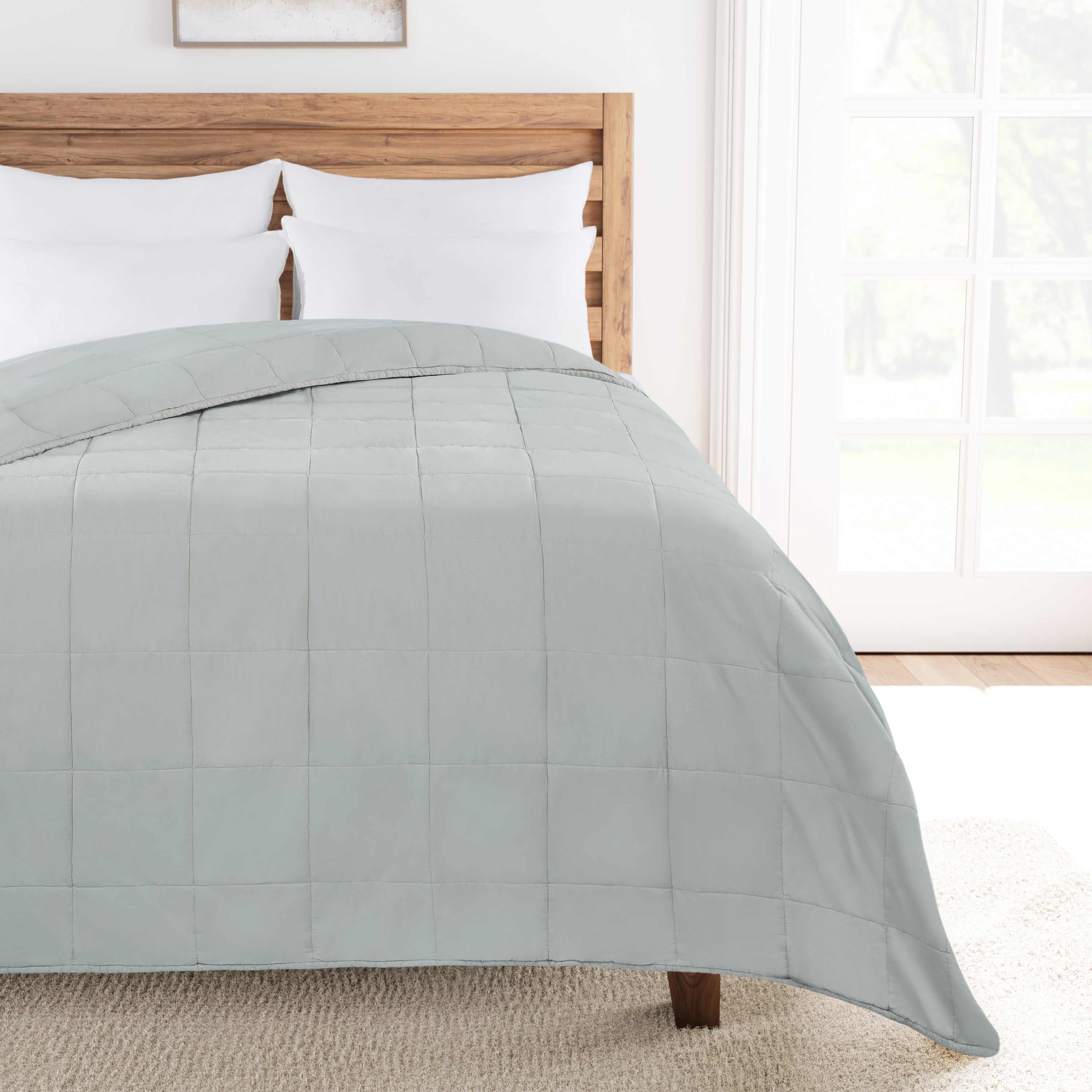 Bed with Oystershell comforter and wooden headboard in a bright room