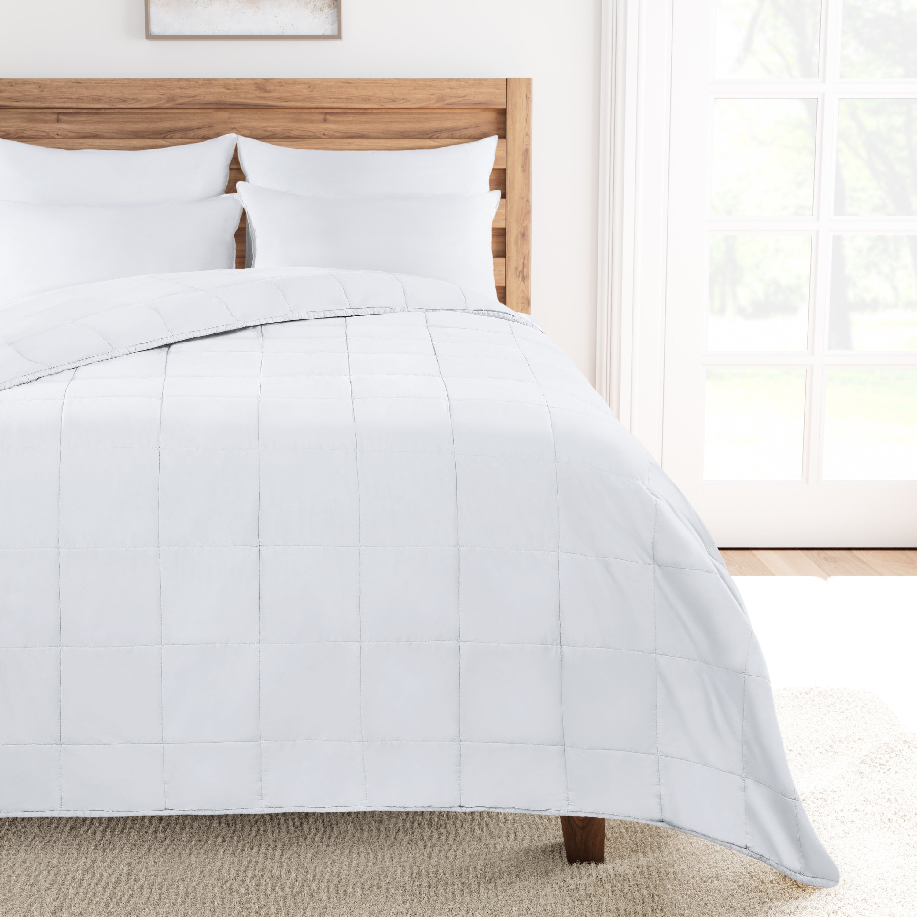 White comforter on a bed with a wooden headboard in a bright room.