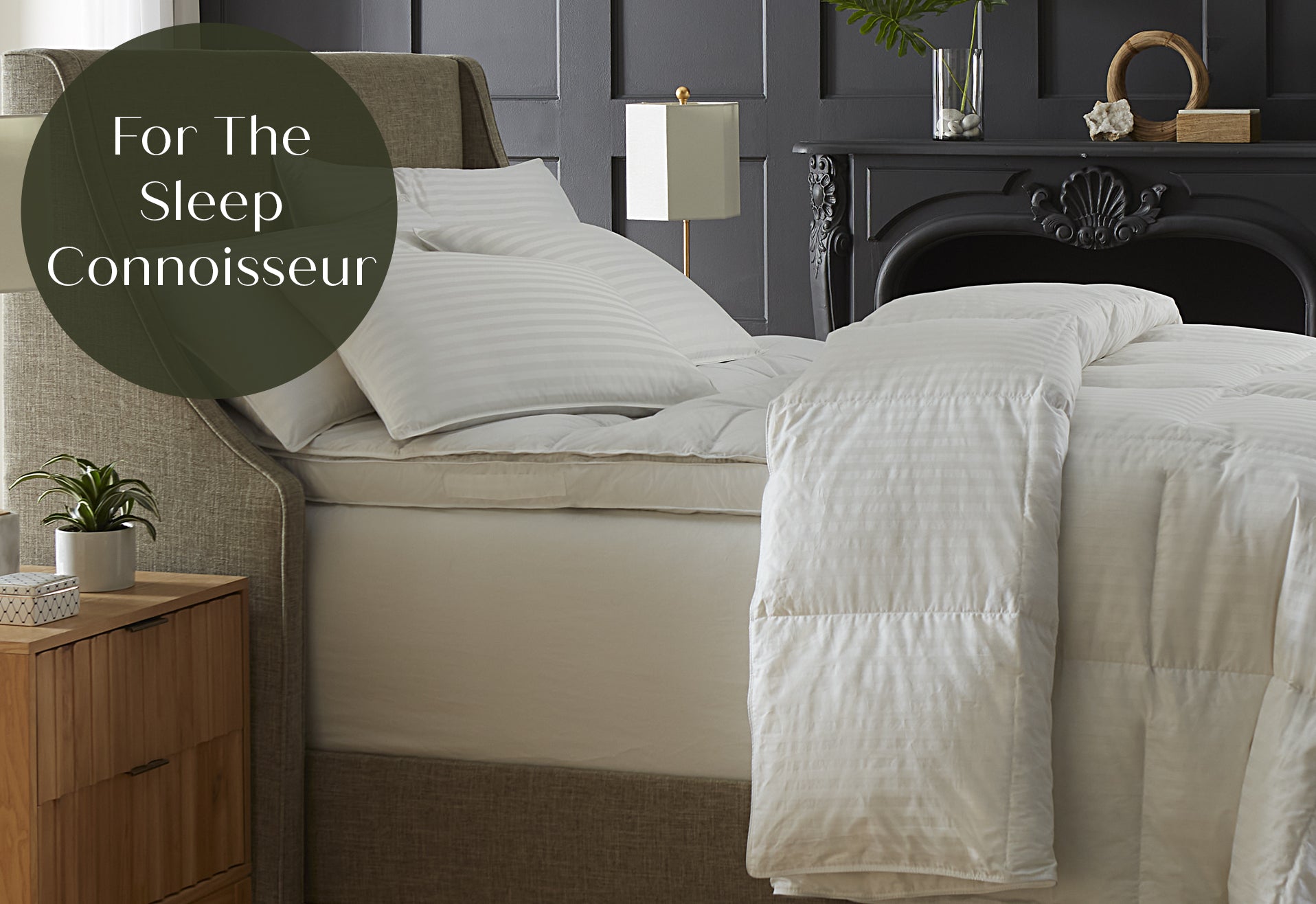 Neatly made bed with white bedding in a bedroom setting, featuring a nightstand and decorative item "for the sleep connoisseur"