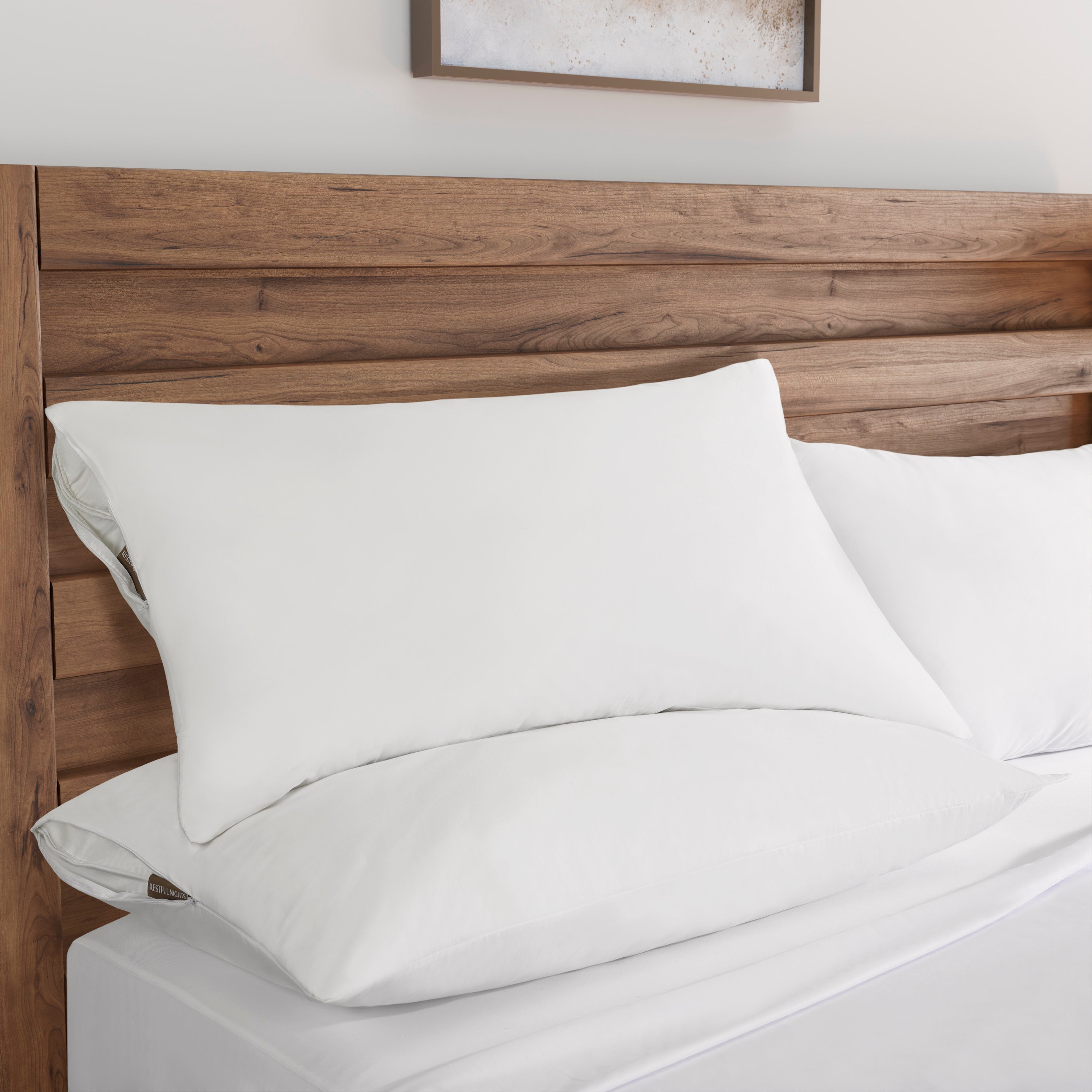 White bed sheets and pillows on a wooden bed frame with a neutral wall and framed picture in the background.