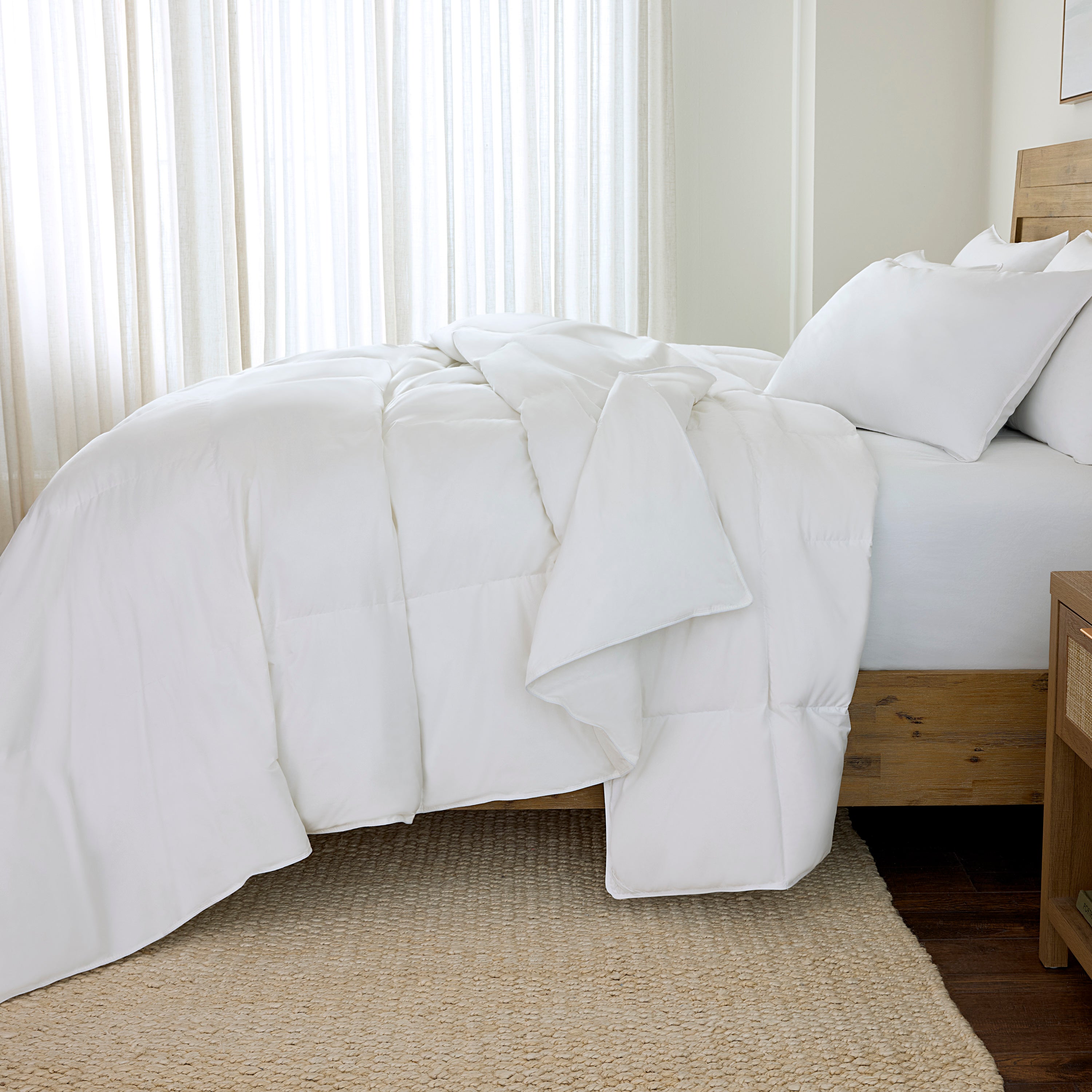 White comforter on a bed in a bedroom with light curtains.