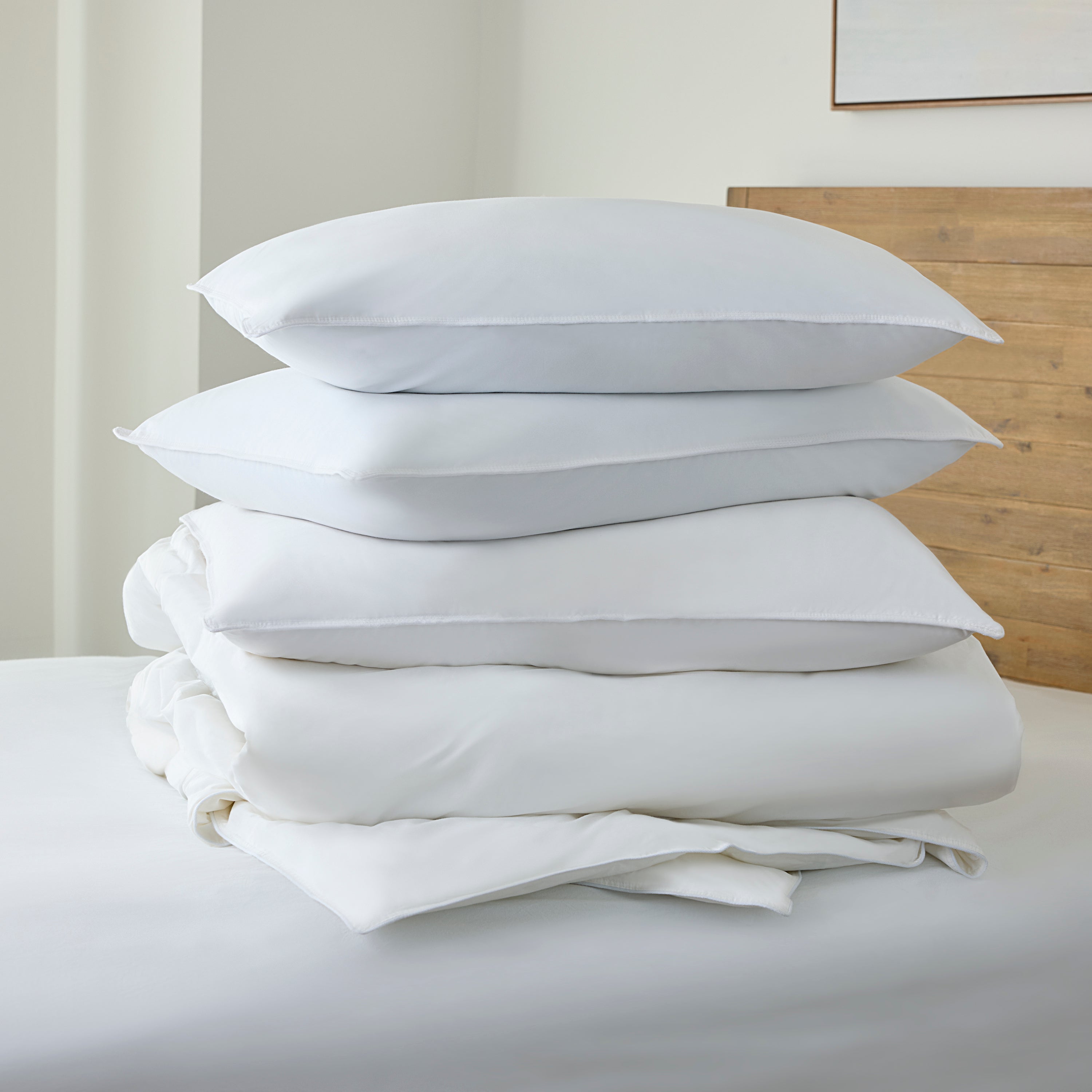 Stack of white pillows and duvet on a bed with a neutral background