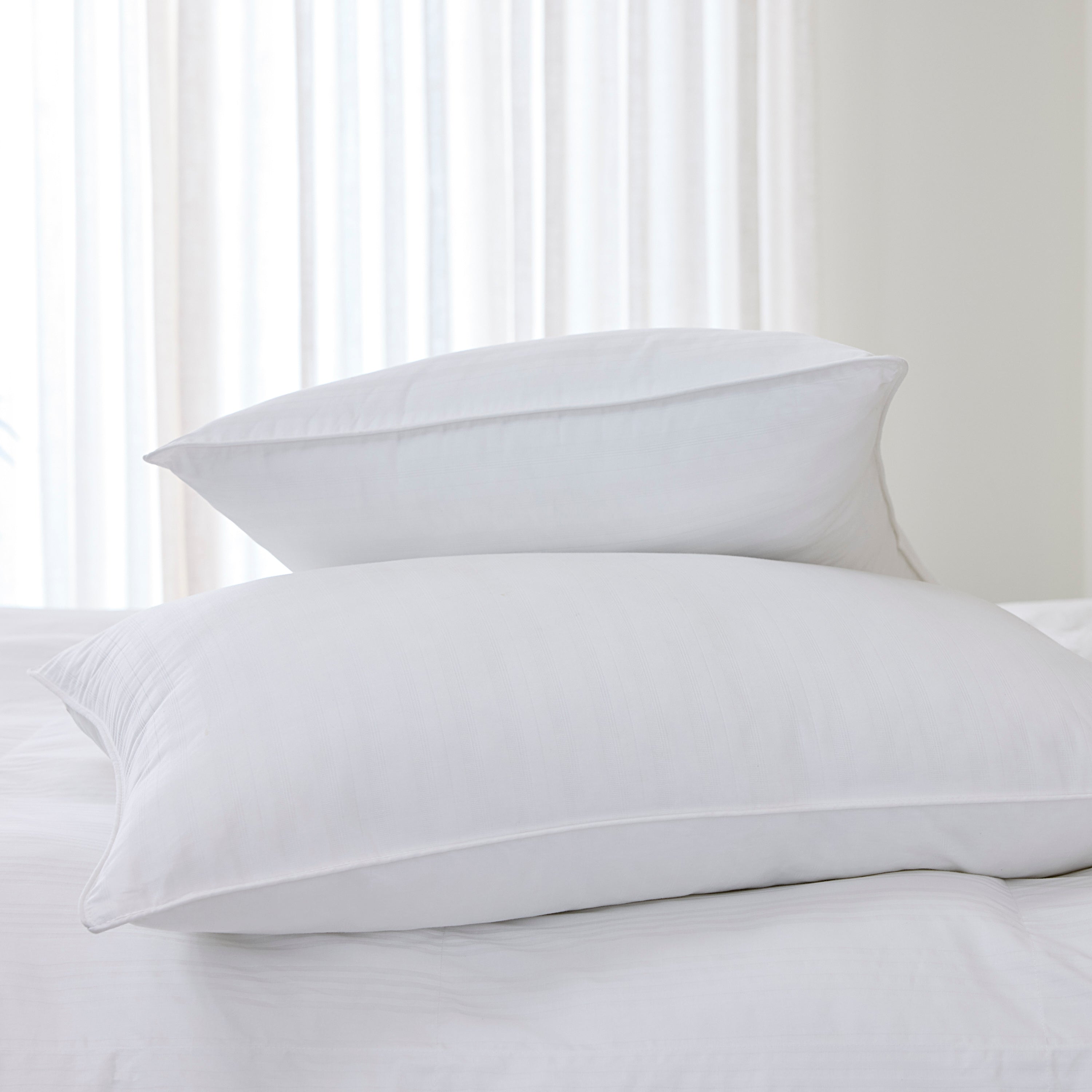 Two white pillows on a bed with a neutral background