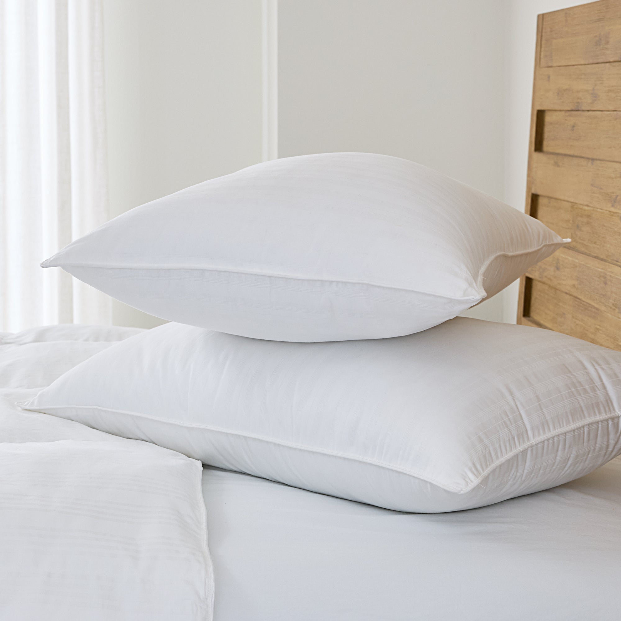 Two white pillows stacked on a bed with a wooden headboard.