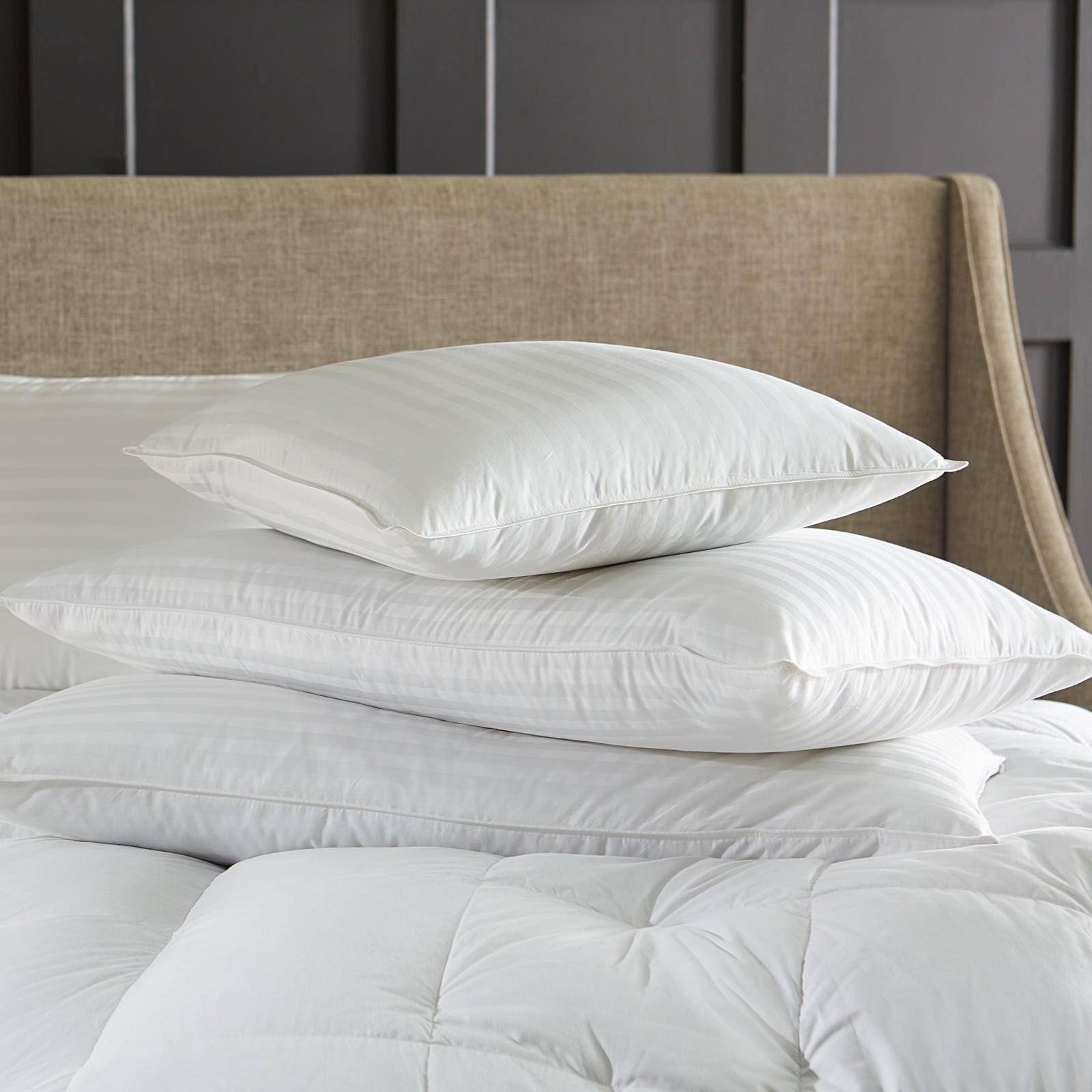 Stack of white pillows on a bed with a beige headboard and nightstand.