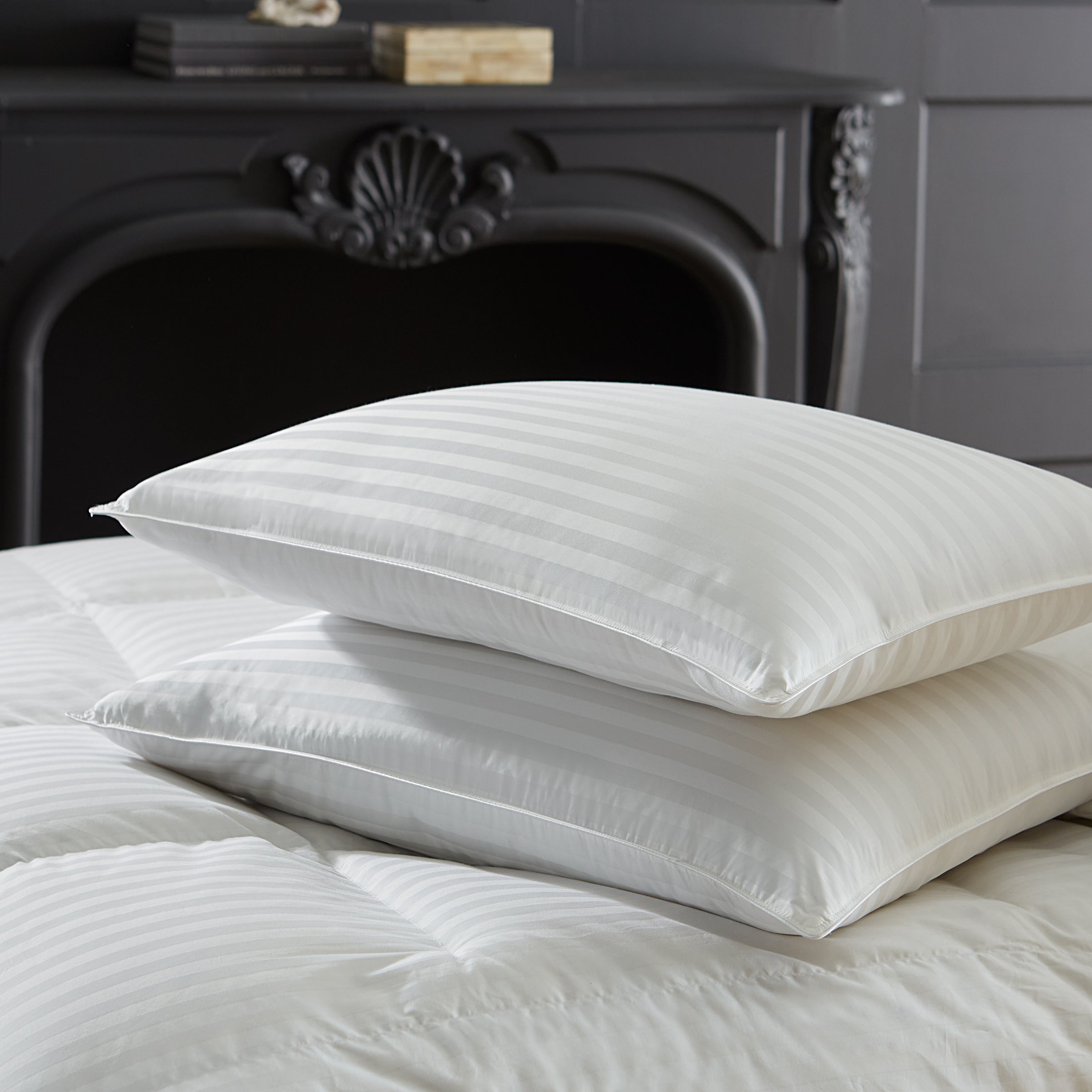Two white pillows on a bed with a decorative fireplace in the background