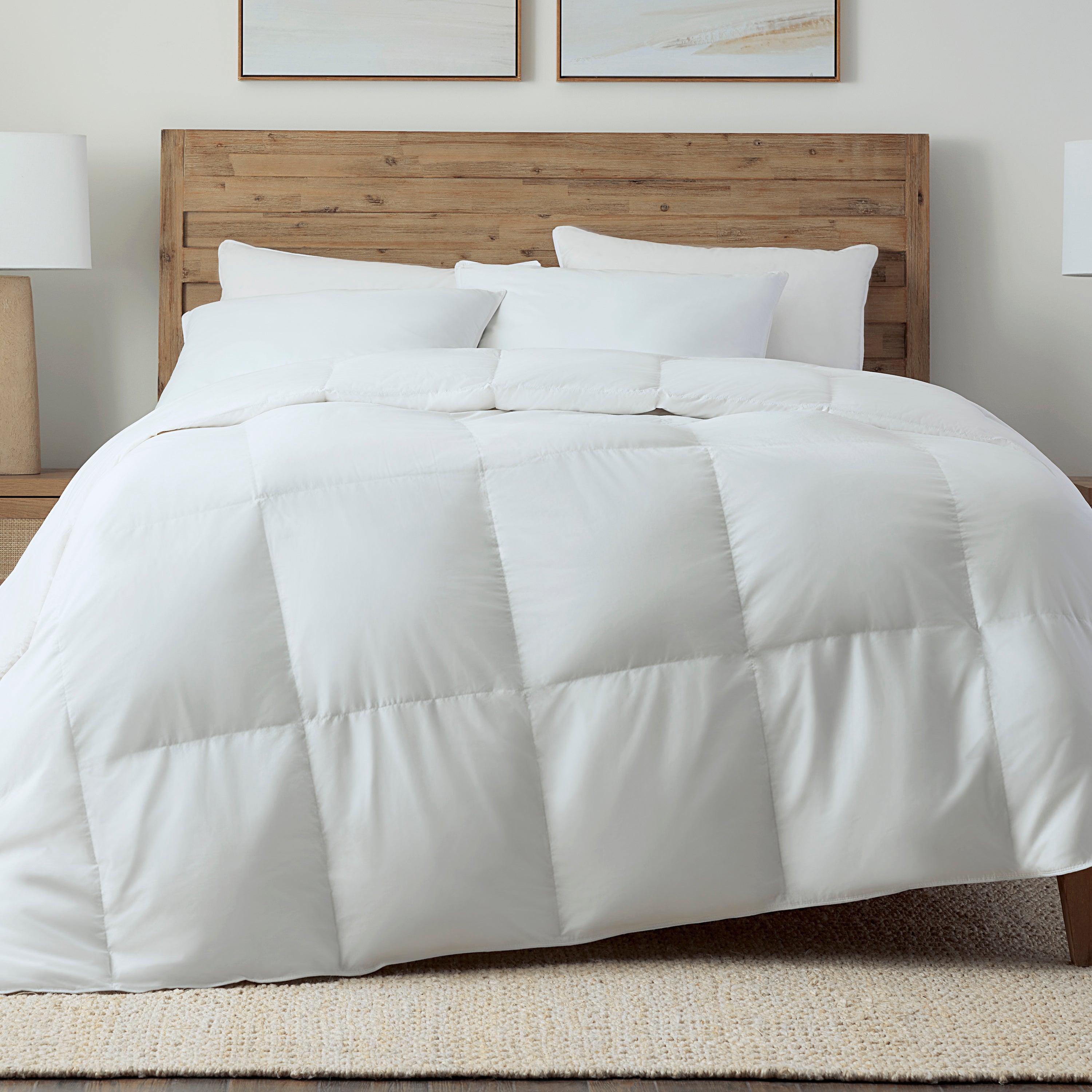 White comforter on a bed with wooden headboard and framed pictures on the wall.