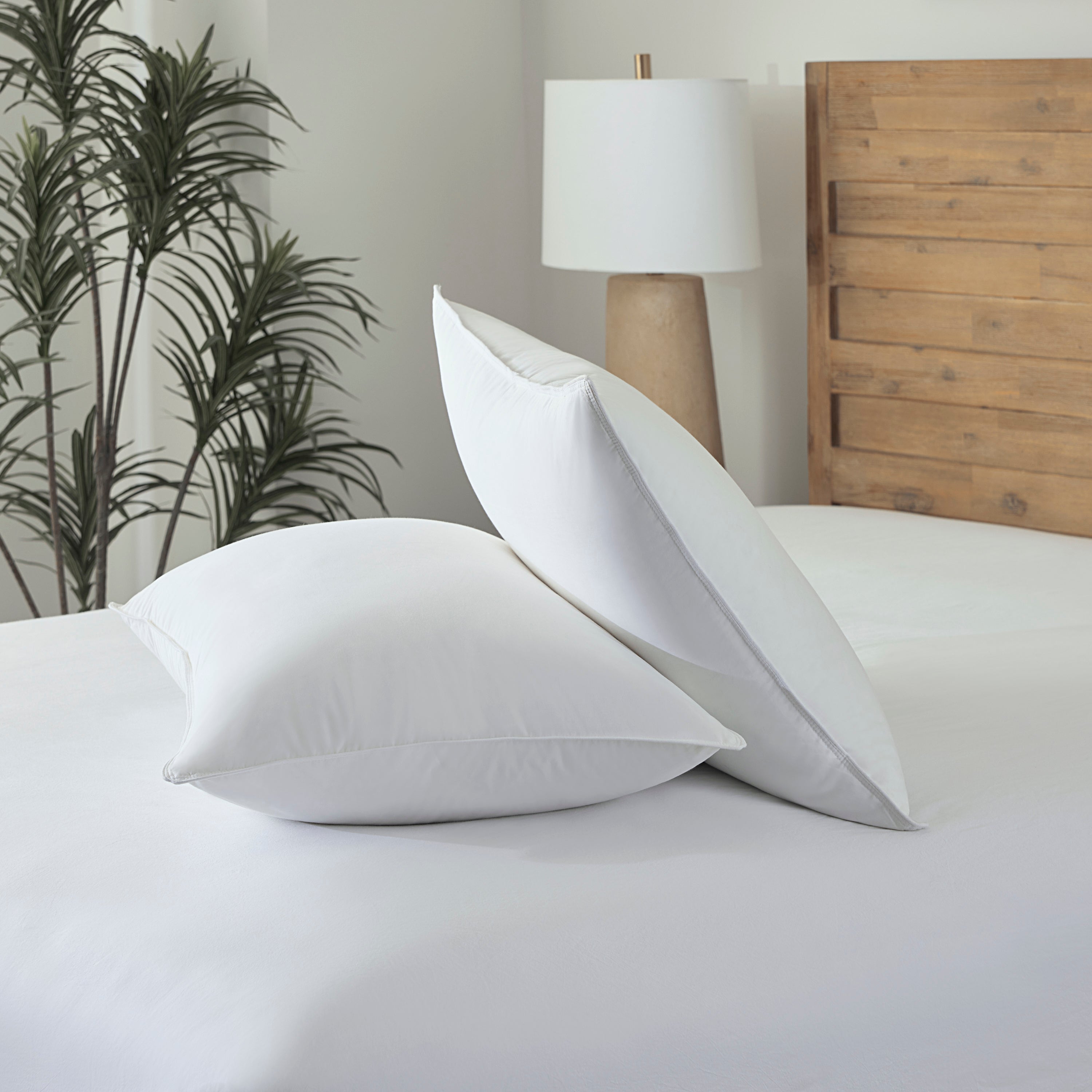 Two white pillows on a bed with a wooden headboard and lamp in the background.